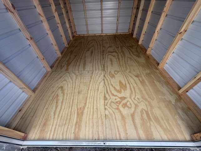 Close-up of real-wood treated plywood flooring inside a DANCO 8×12 utility shed, showing wood grain and panel seams.